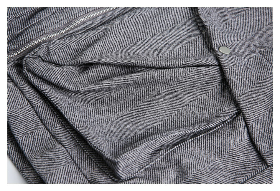 Close-up of a gray herringbone jacket with a folded pocket flap, zipper, and metal snap.