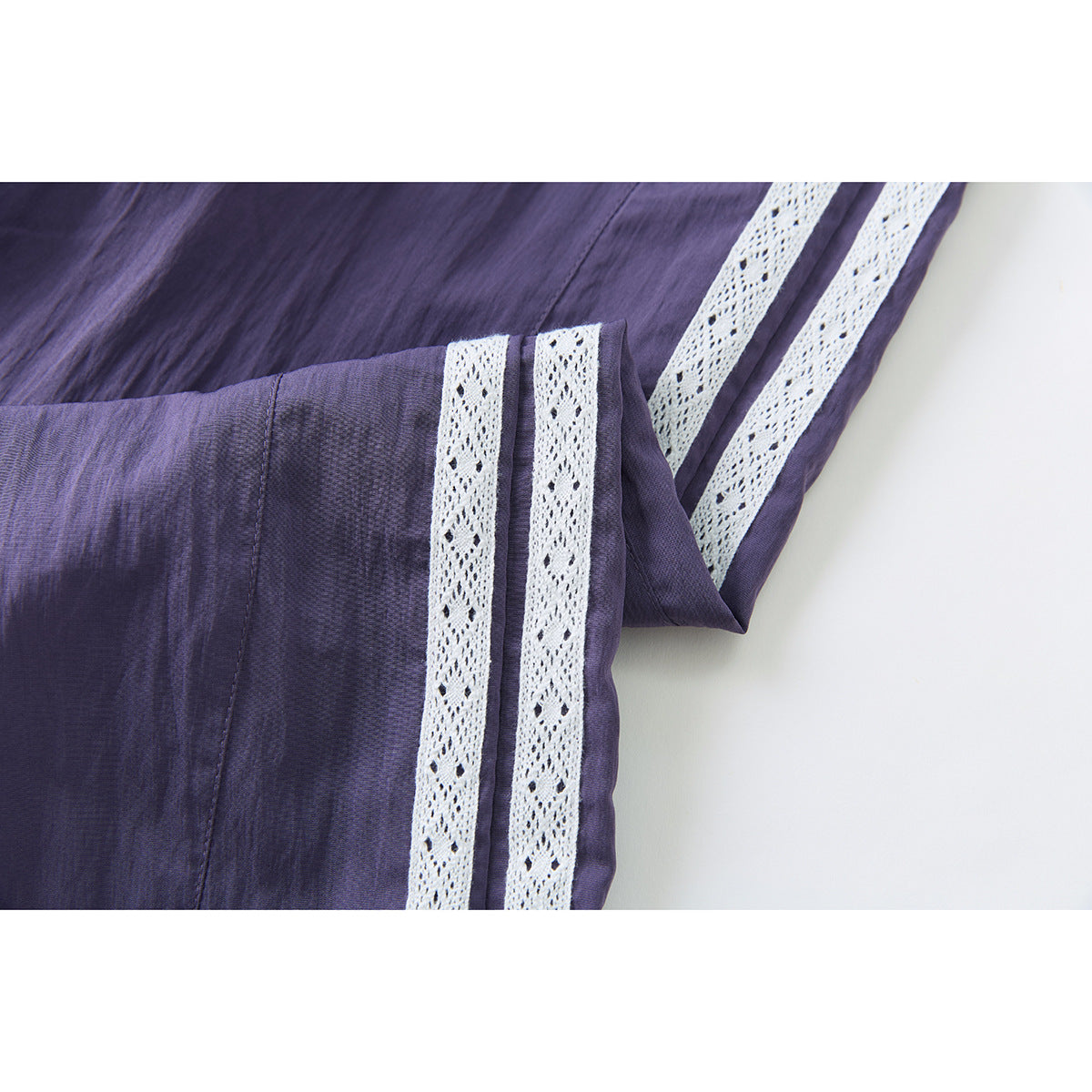 Close-up of purple pants showing white lace side stripes and the fabric texture.