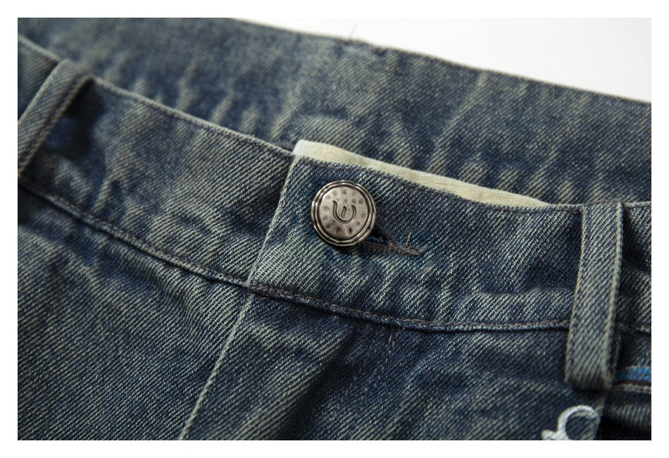 Close-up of the jeans' metal waistband button and faded blue denim stitching.