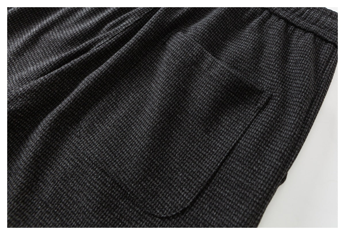 Close-up of dark gray patterned trousers showing a curved side pocket and stitching.