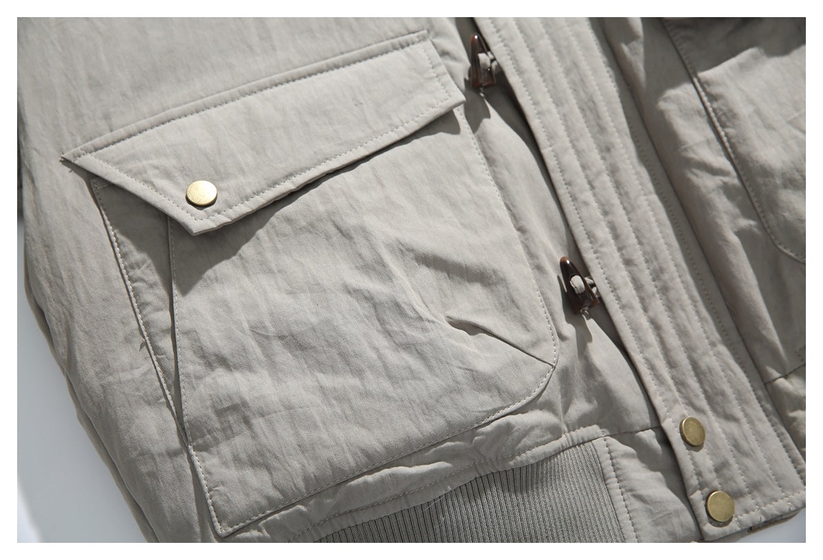 Close-up of a light taupe jacket with a large flap pocket, brass-tone snaps and toggle fasteners.