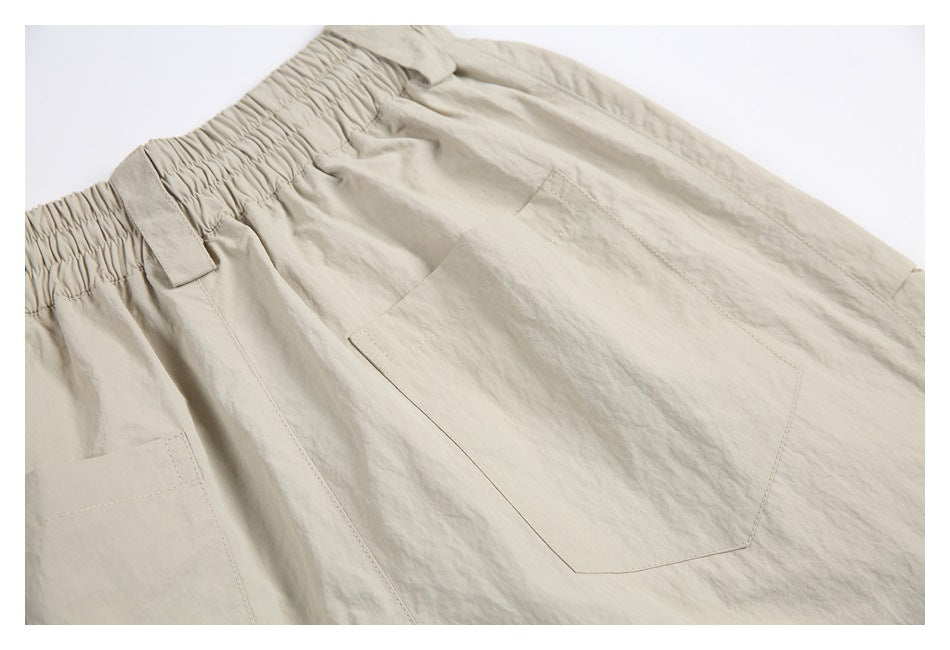 Angled close-up of light beige bottoms with a gathered elastic waistband, belt loops, and patch pockets.