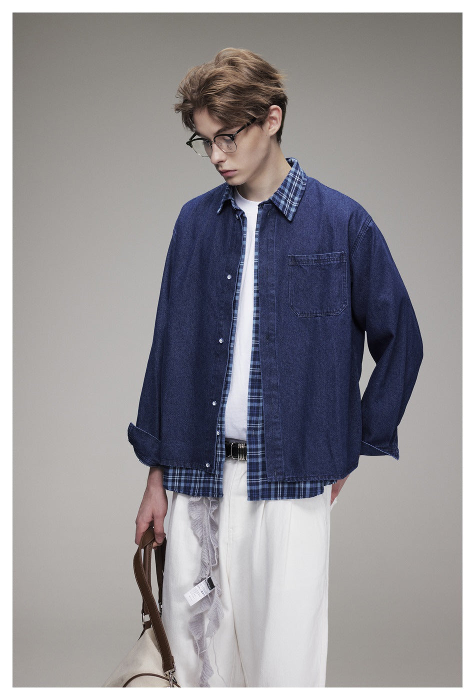 Model looking down in a navy denim overshirt layered over a blue plaid shirt and white trousers.