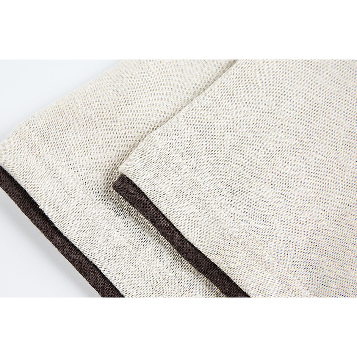 Close-up of a cream shirt hem with dark brown contrast trim and visible stitching.