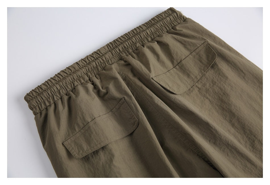 Close-up of olive-brown pants showing an elastic waistband and two flap pockets.
