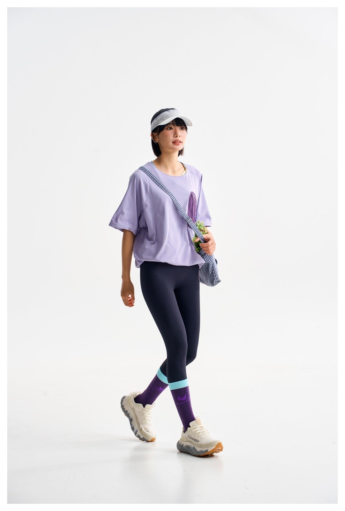 Model walking in a lavender oversized tee, dark leggings and purple socks with turquoise bands.
