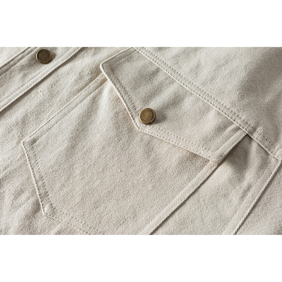 Close-up of a beige shirt chest pocket with a flap and brass button.
