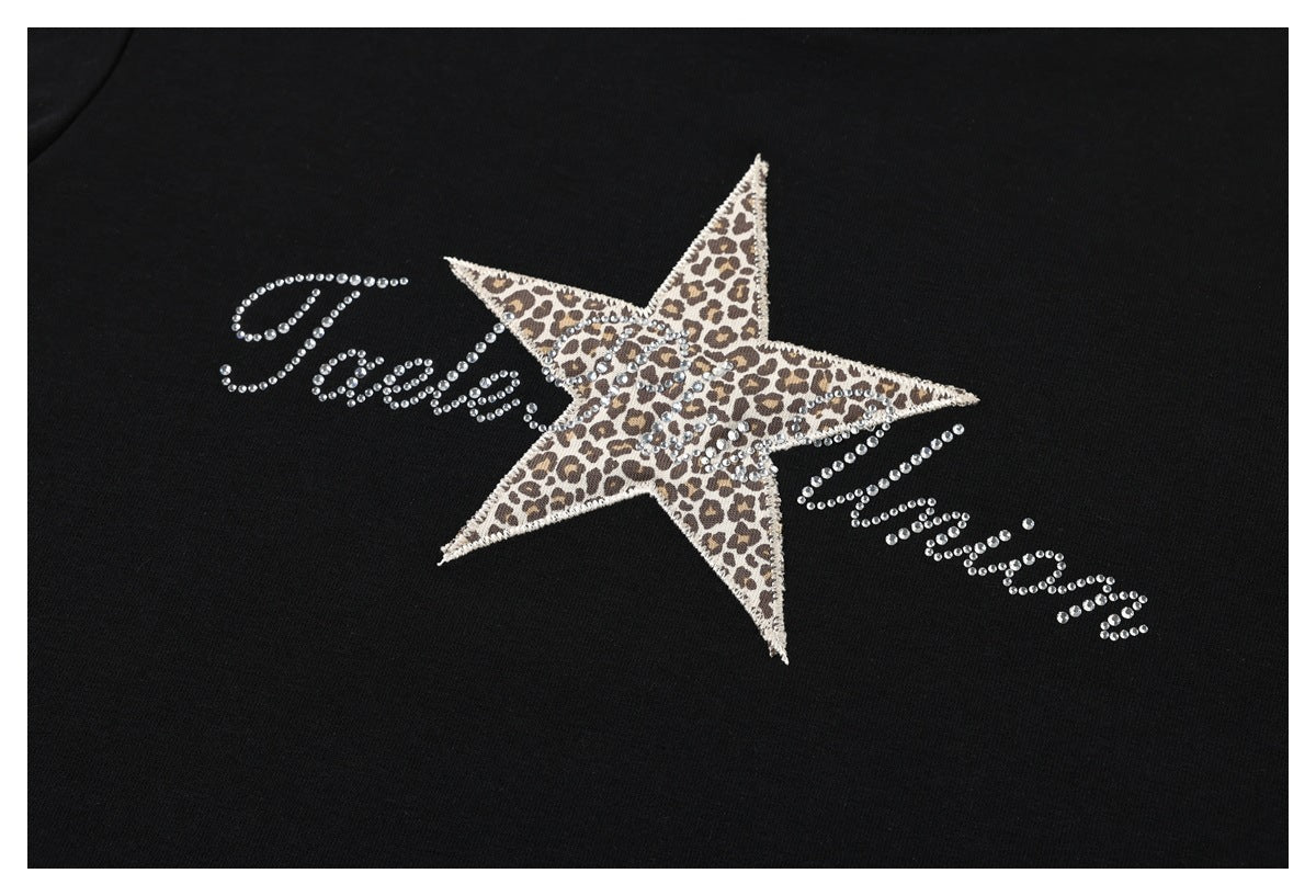Close-up of a leopard-print star and rhinestone script decoration on black T-shirt fabric.