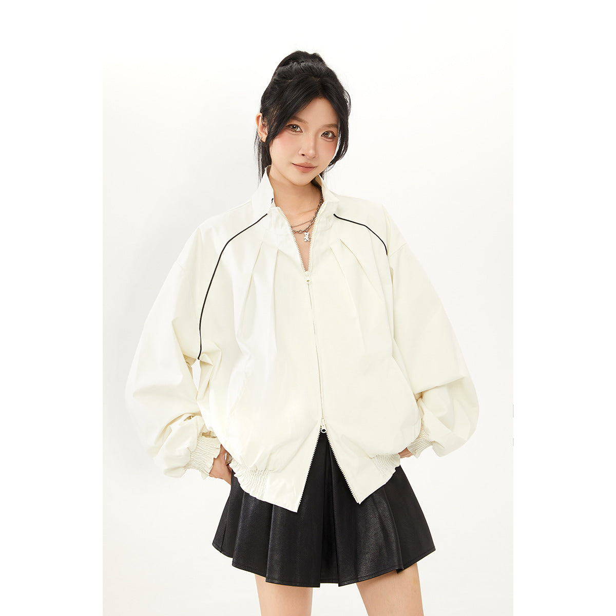 Model wearing an ivory zip-up jacket with black piping and voluminous sleeves over a black flared skirt.