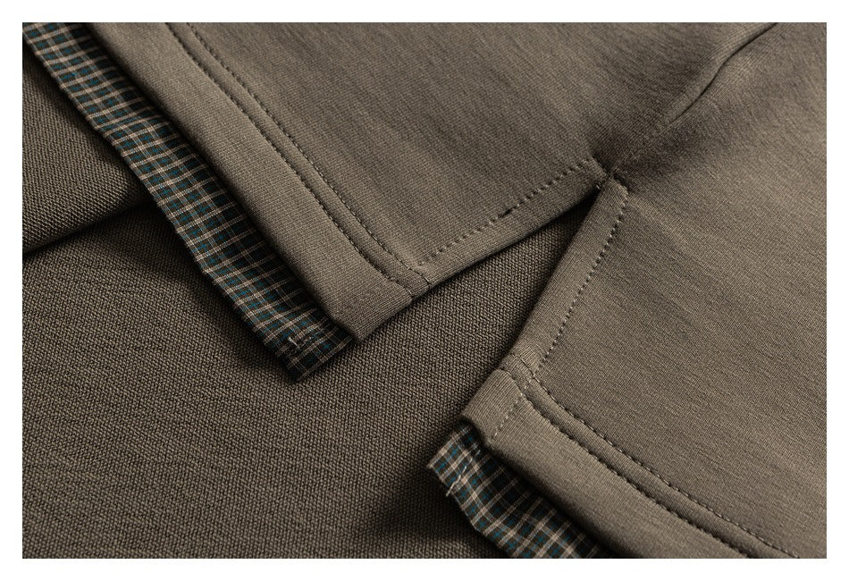 Close-up of taupe garment seams and hems with narrow green-and-brown plaid trim.