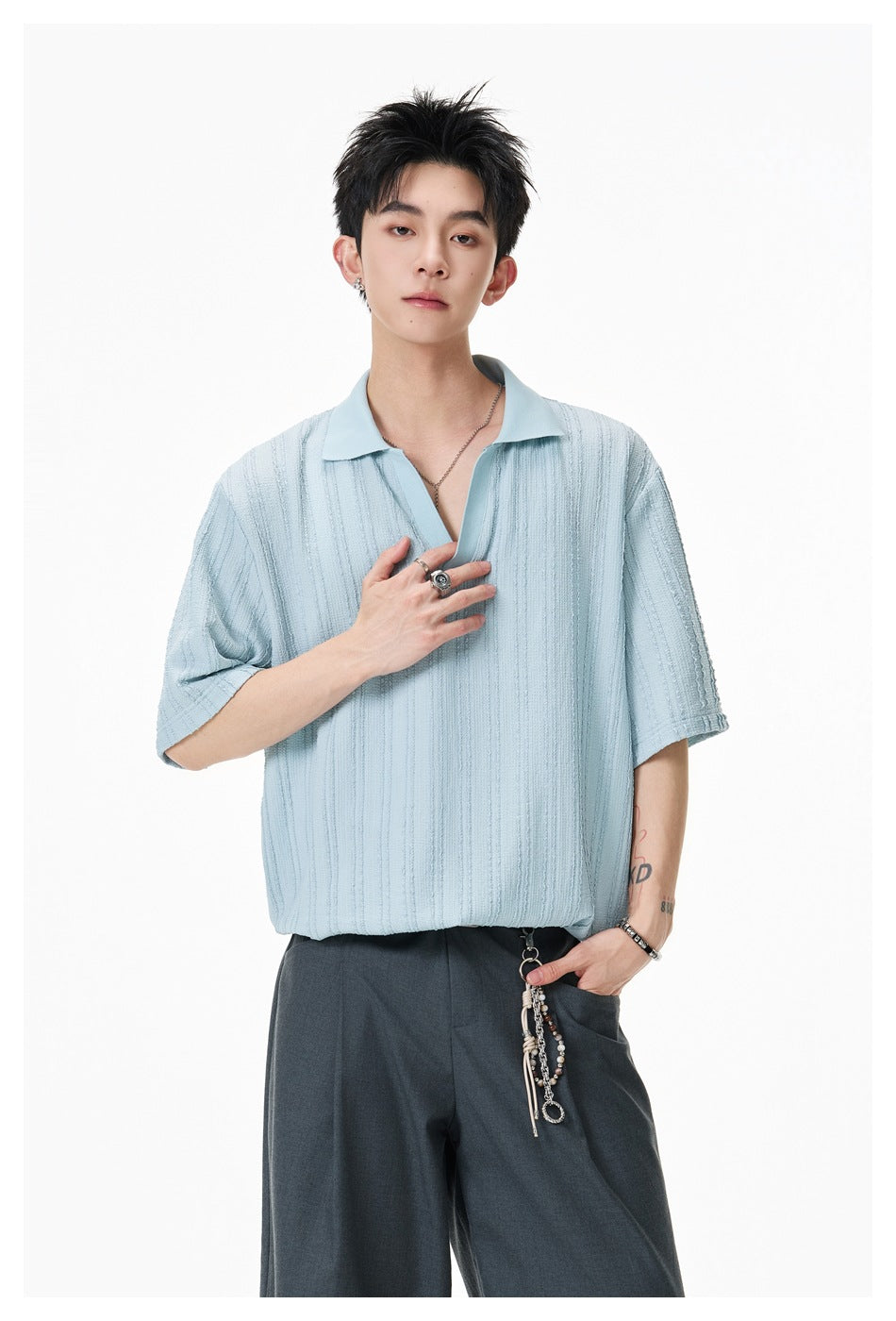 Model wearing a pale blue textured short-sleeve polo with dark wide-leg trousers.