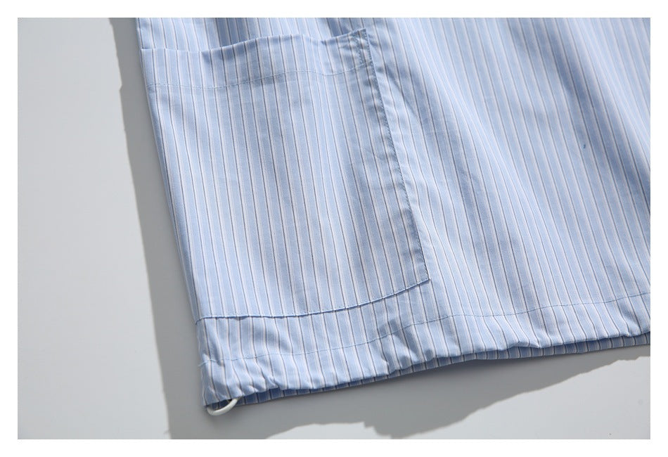 Close-up of a light blue pinstriped shirt showing a patch pocket and stitched hem.