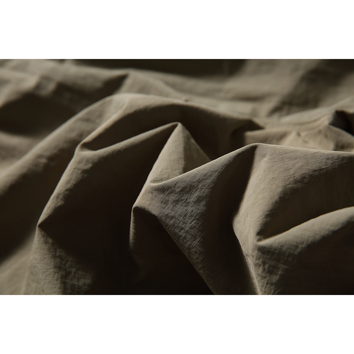 Macro view of the softly crumpled, subtly gridded taupe shorts fabric.