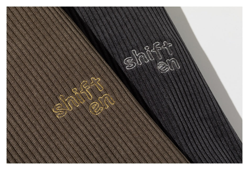 Close-up of taupe and black ribbed jackets with embroidered lettering on the chest.