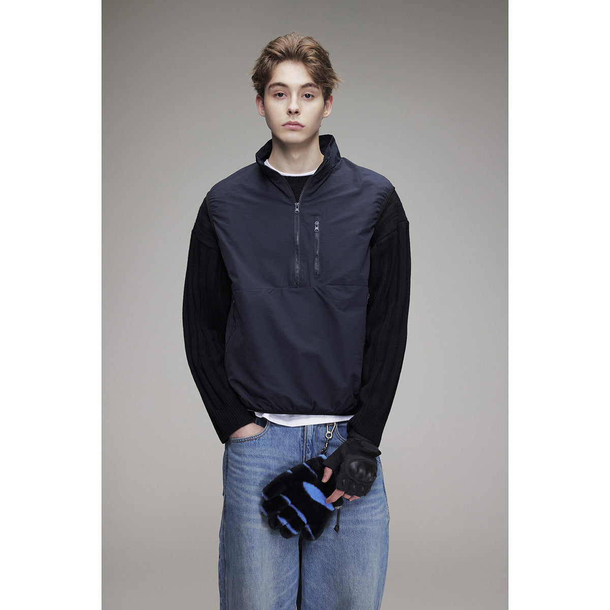 Front view of a model wearing a navy zip-front vest with a high collar and zip pockets over black sleeves.