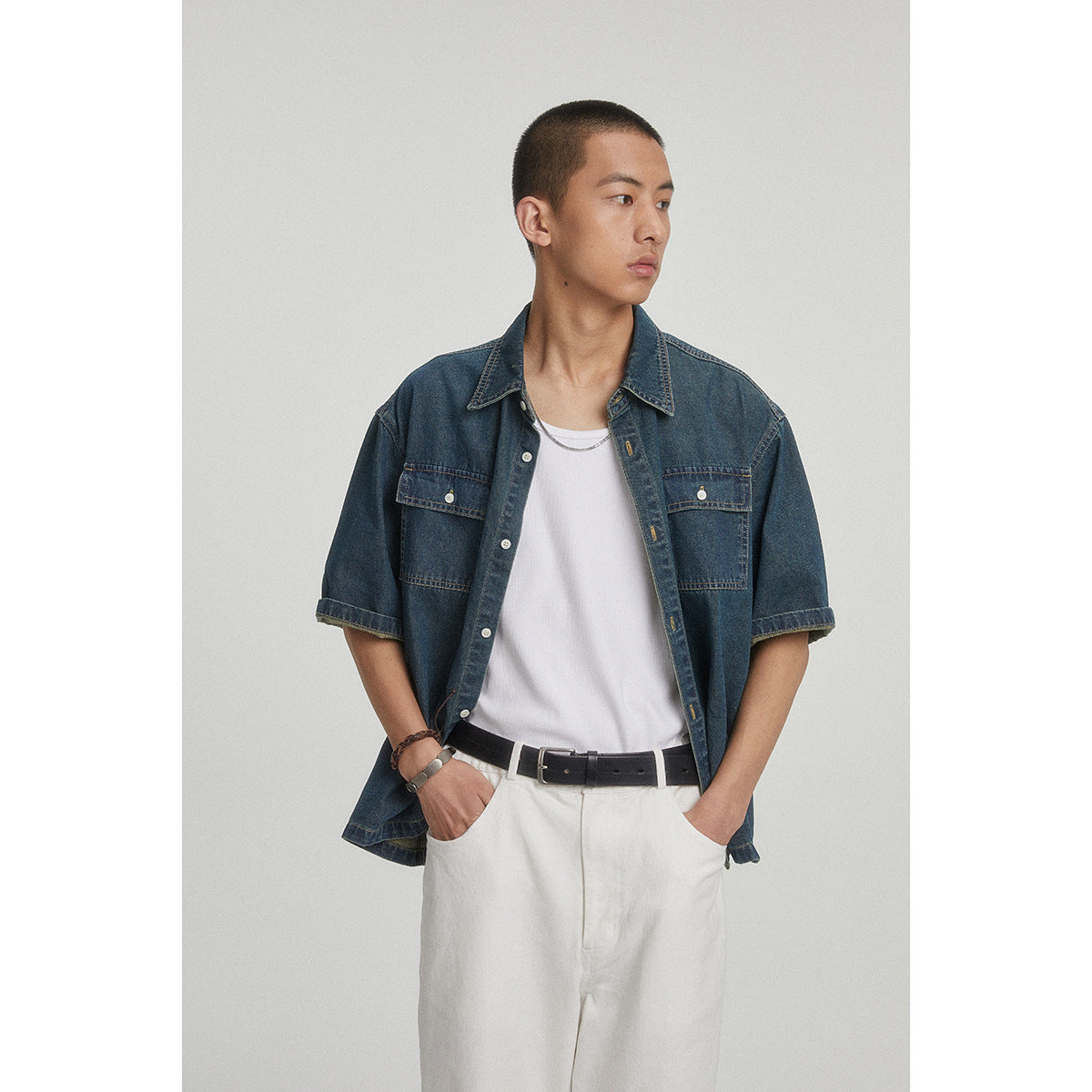 Closer front view of a model wearing an open dark blue denim shirt with two button-flap chest pockets over a white tee.