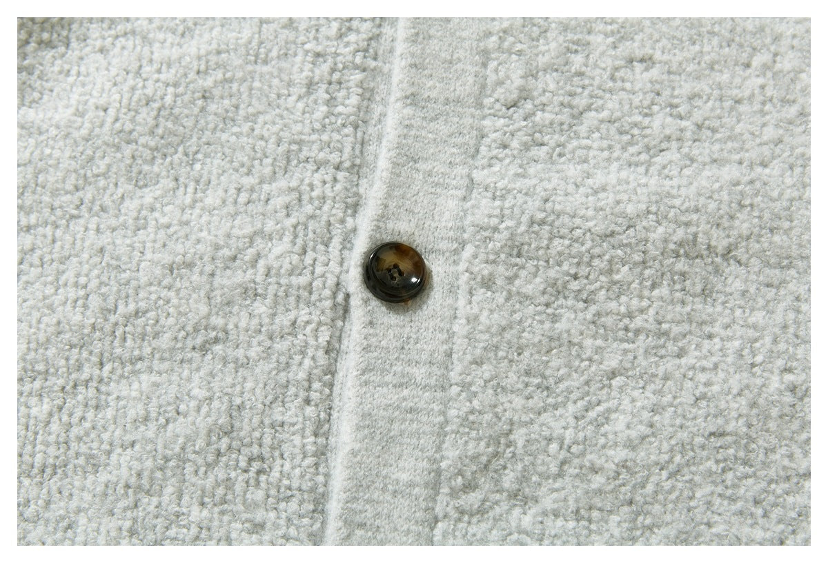 Close-up of a dark brown button on the placket of a light gray textured knit sweater.