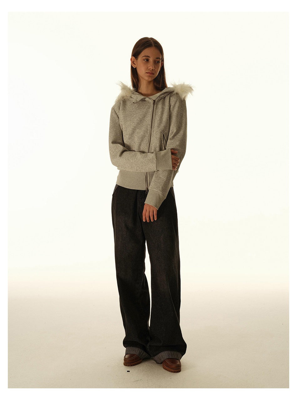 Three-quarter view of a model wearing a light gray fur-trimmed hooded zip jacket and wide black pants.