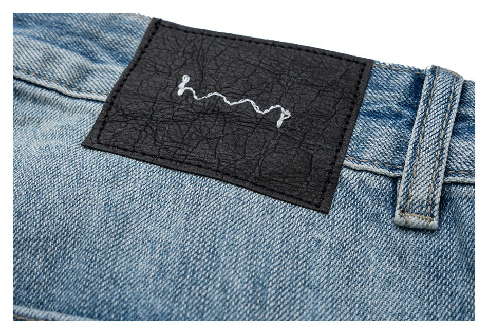 Close-up of a black textured waistband patch with white abstract stitching on light blue denim.