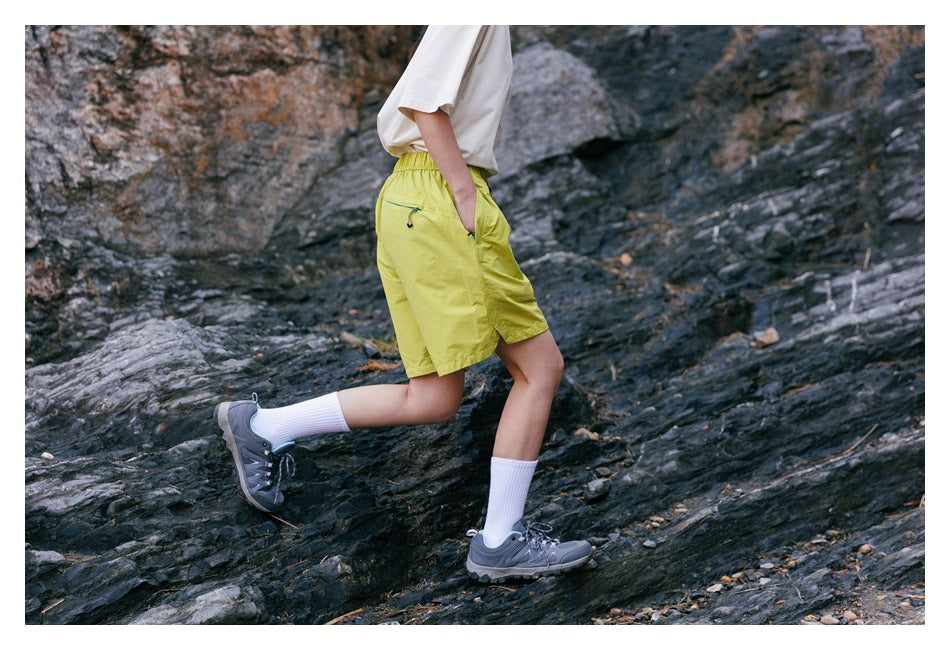 Side and rear view of a person wearing yellow-green shorts with a rear zip pocket on rocky terrain.