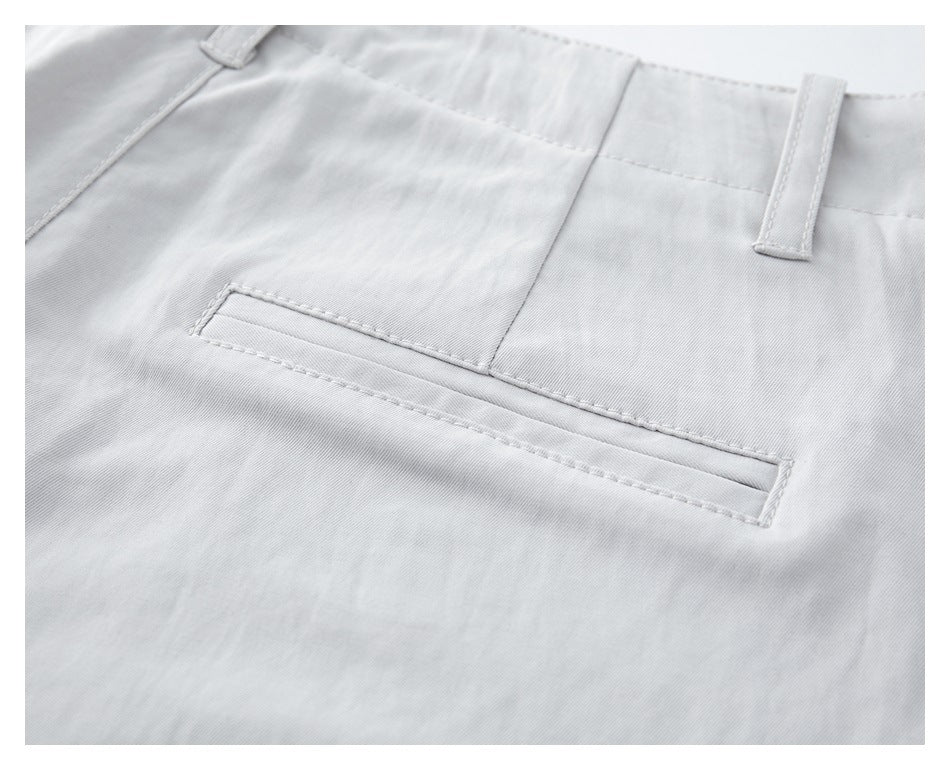 Close-up of white trousers showing a narrow welt pocket and belt loops.
