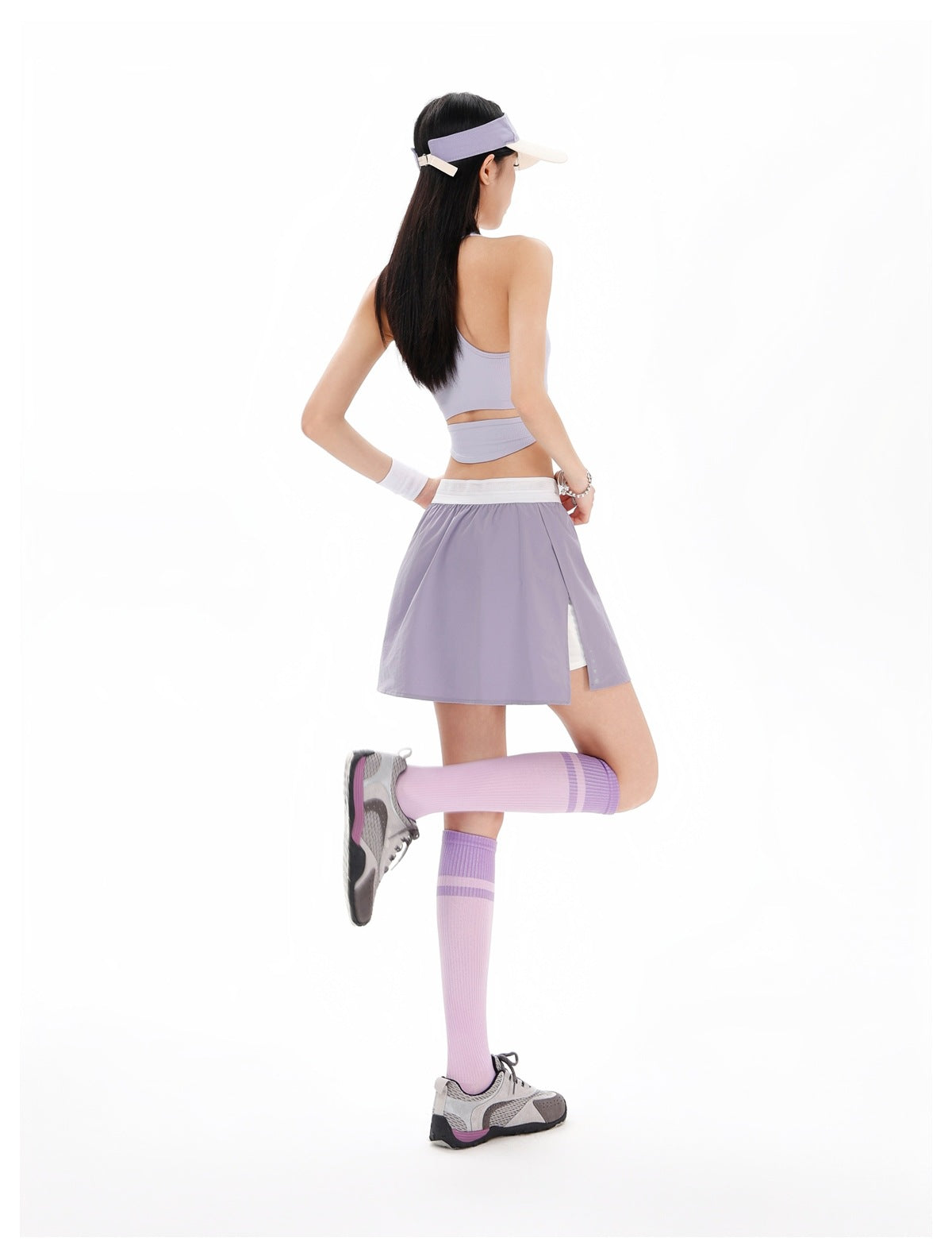 Rear view of a model wearing a lavender tennis skirt with white waistband and matching lilac athletic top.