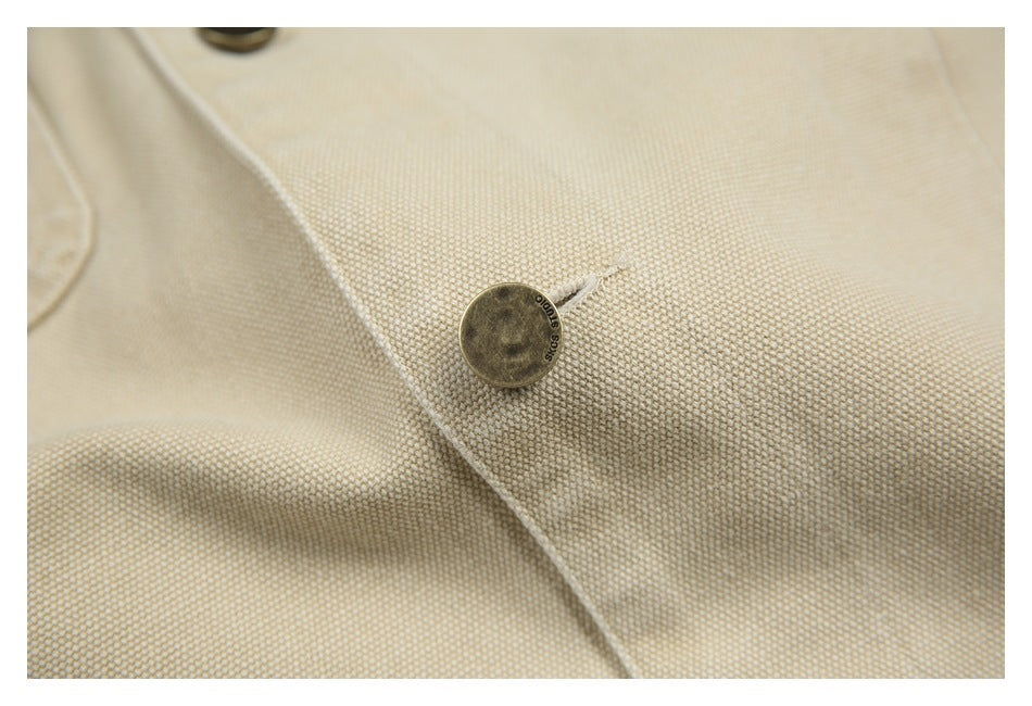 Close-up of a round metal button on the textured beige jacket fabric.
