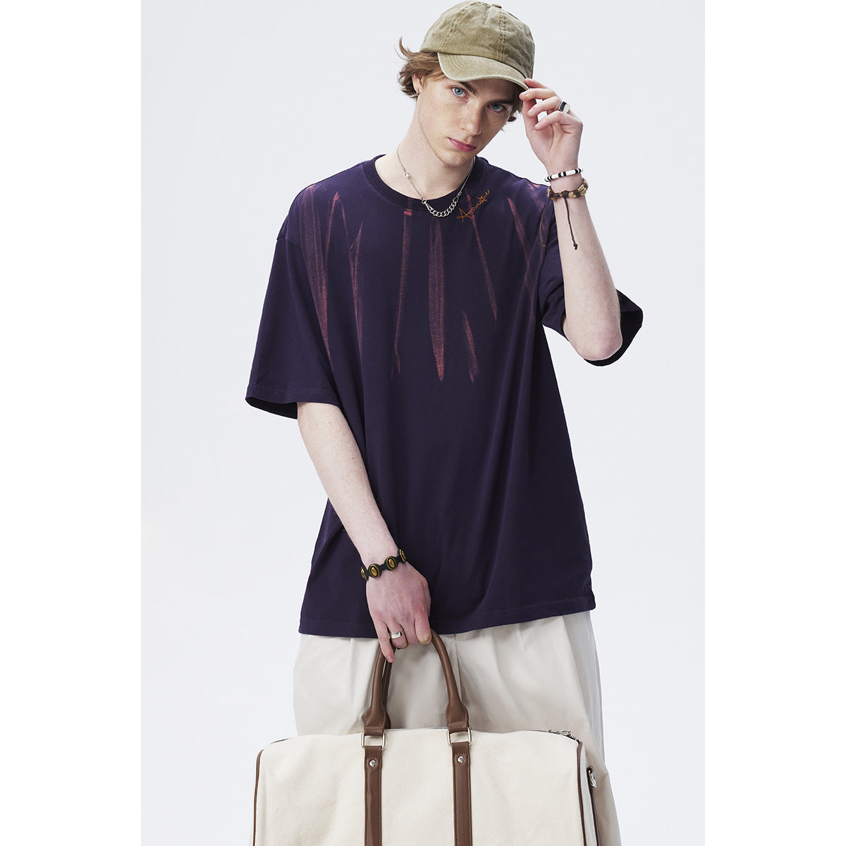 Model wearing an oversized dark purple T-shirt with faded vertical graphics and white trousers, shown from the front.