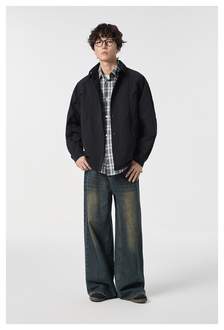 Front view of a model wearing a black collared snap-front jacket over a plaid shirt.