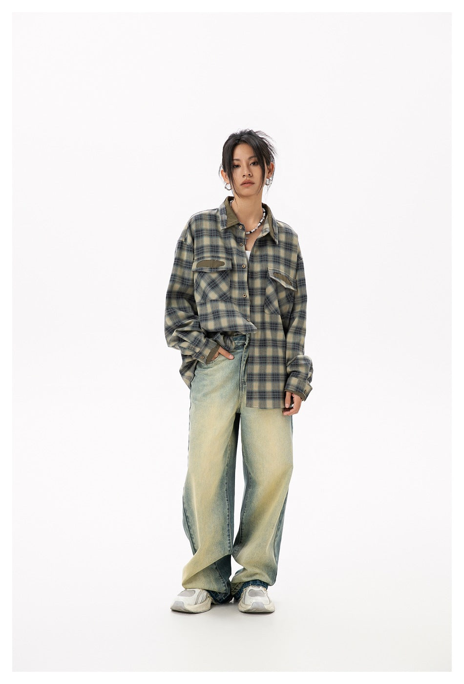 Model wearing green plaid shirt with chest flap pockets, hand in jeans pocket, with faded wide-leg jeans and sneakers
