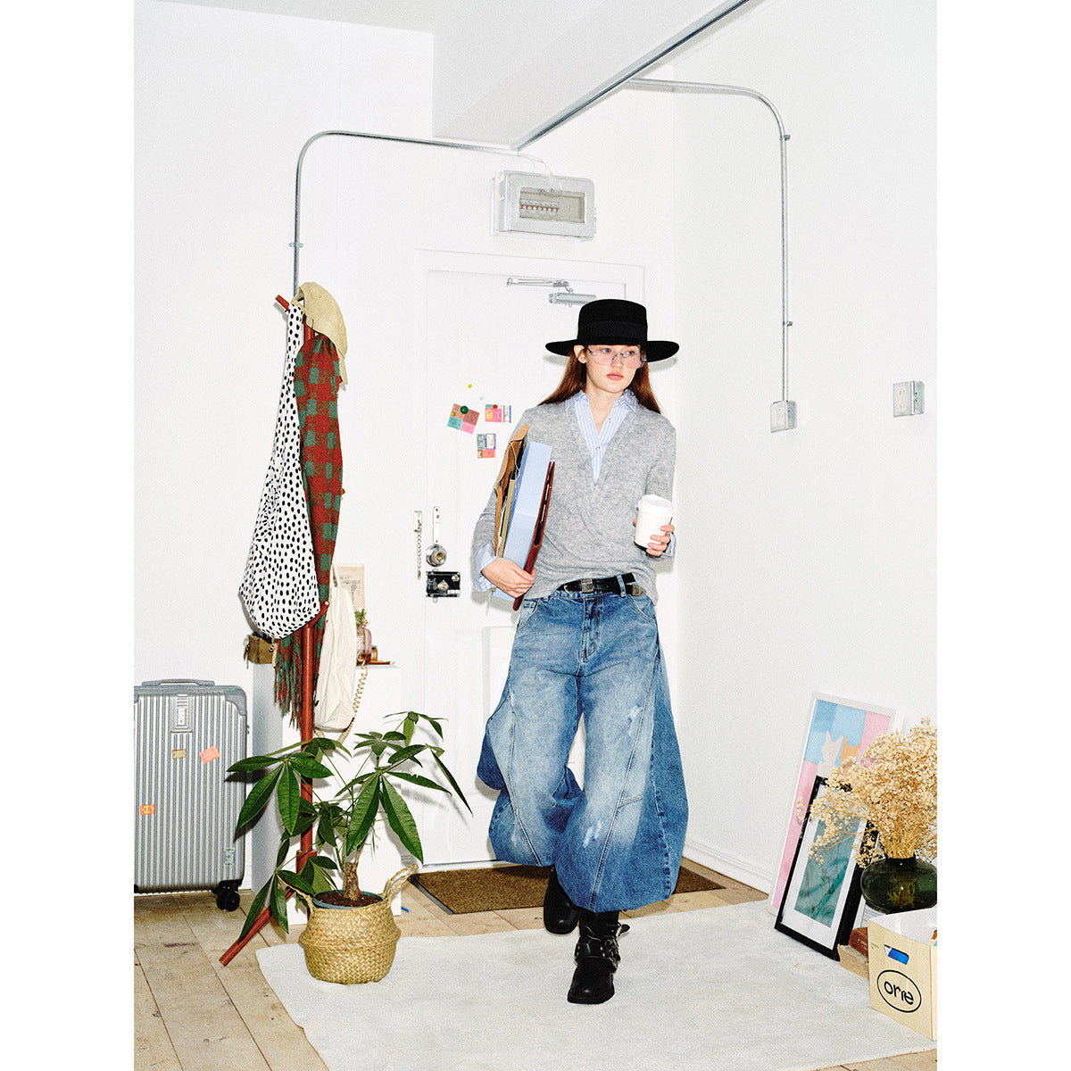 Full-length model wearing a light gray V-neck sweater layered over a blue striped shirt with wide-leg jeans and a black hat.