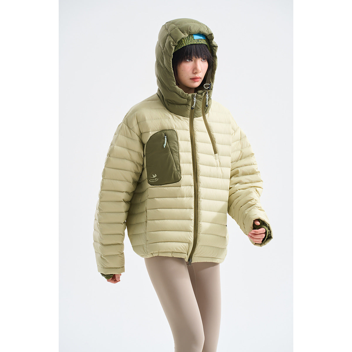 Model wearing a pale sage quilted hooded jacket with an olive hood, front pocket and full-length zip.
