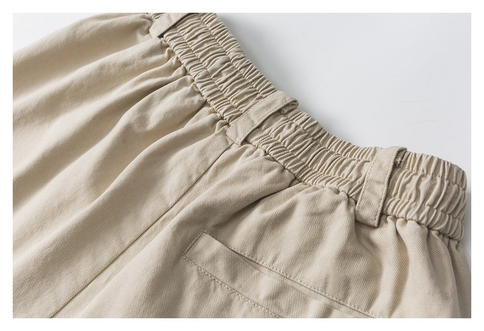 Close-up of beige trousers showing a gathered elastic waistband, belt loops, and pocket stitching.