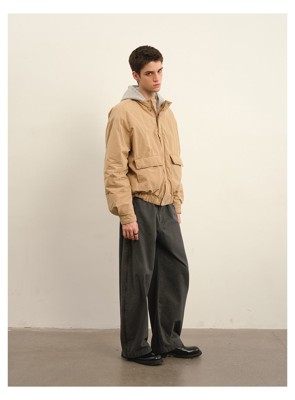 Side-angle view of a model wearing a tan hooded jacket with flap pockets and wide charcoal trousers.