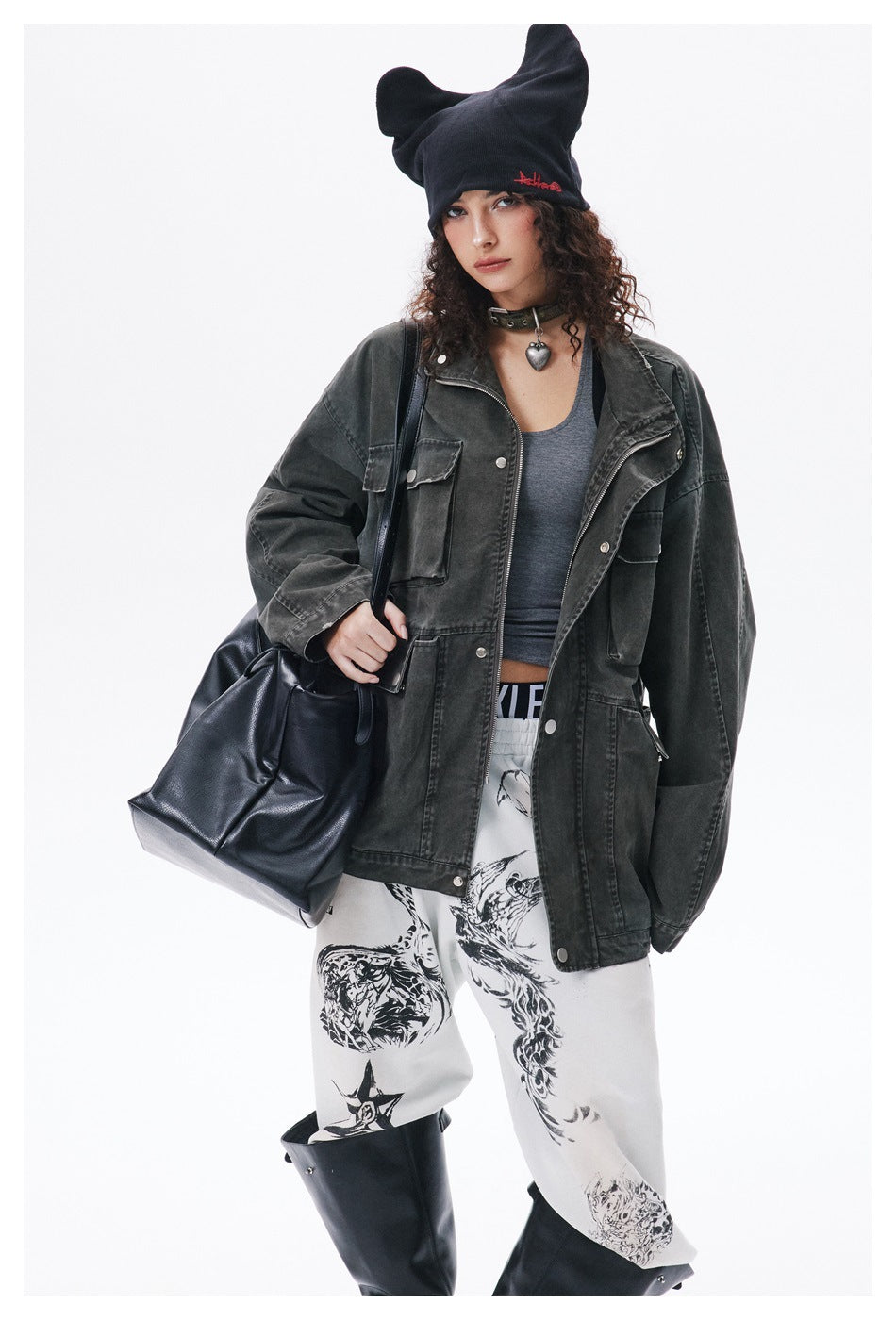 Model wearing an oversized charcoal utility jacket over a gray top with white graphic pants and a black tote.