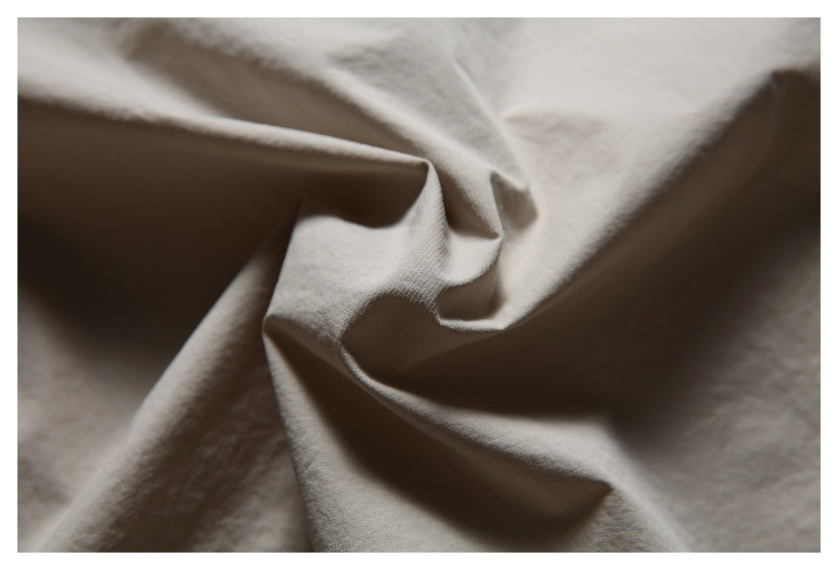 Macro view of light taupe shirt fabric arranged in folds, showing its surface texture.