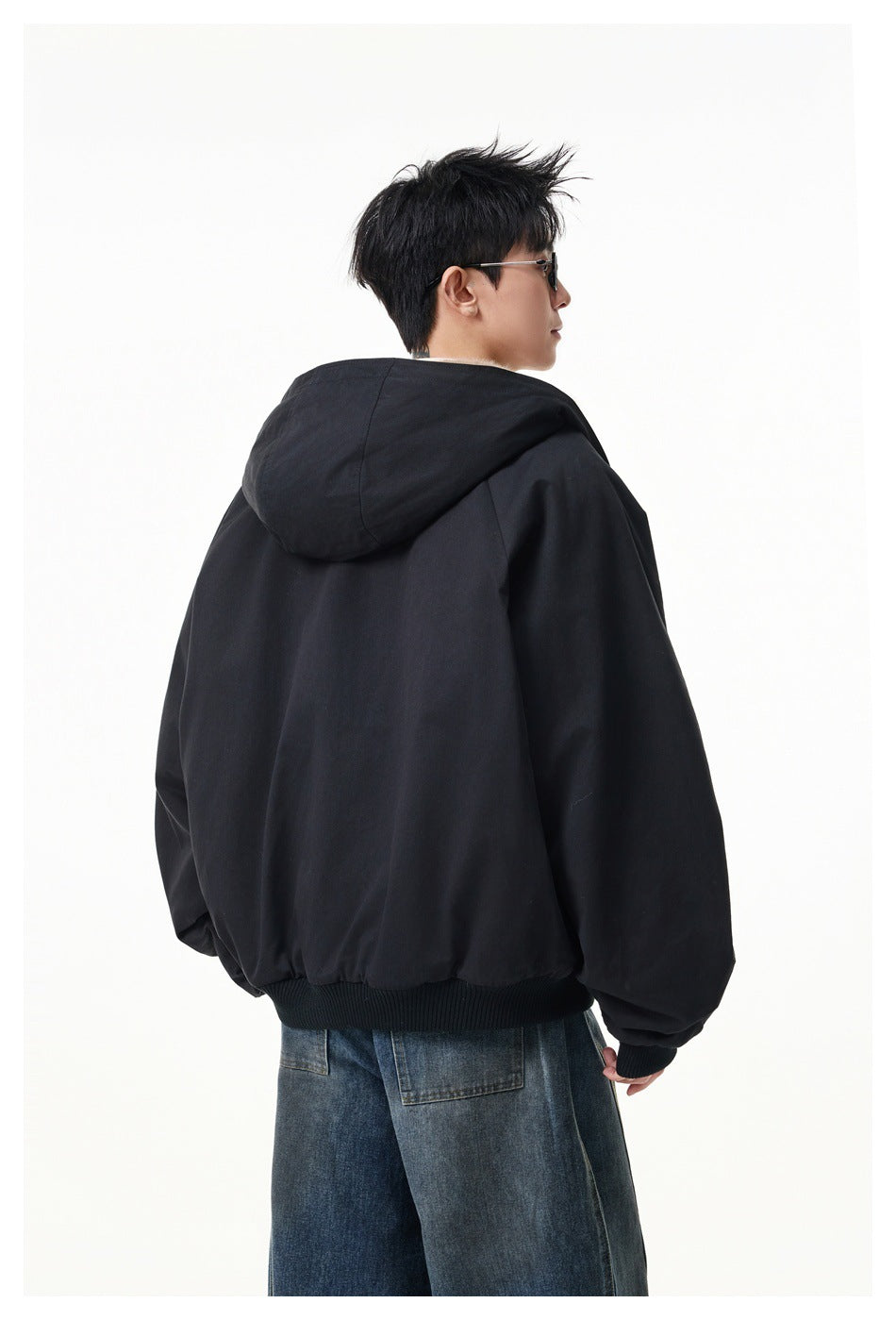 Back view of a man wearing a black hooded jacket with raglan sleeves and a ribbed hem, with wide-leg jeans