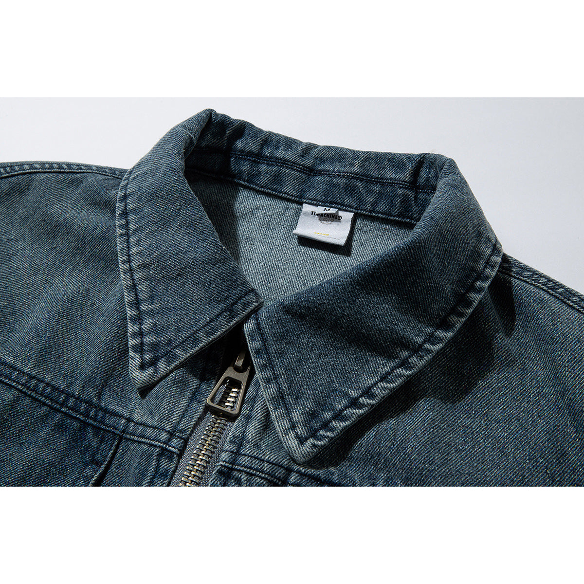 Close-up of a blue denim jacket collar, neck label, and metal front zipper.