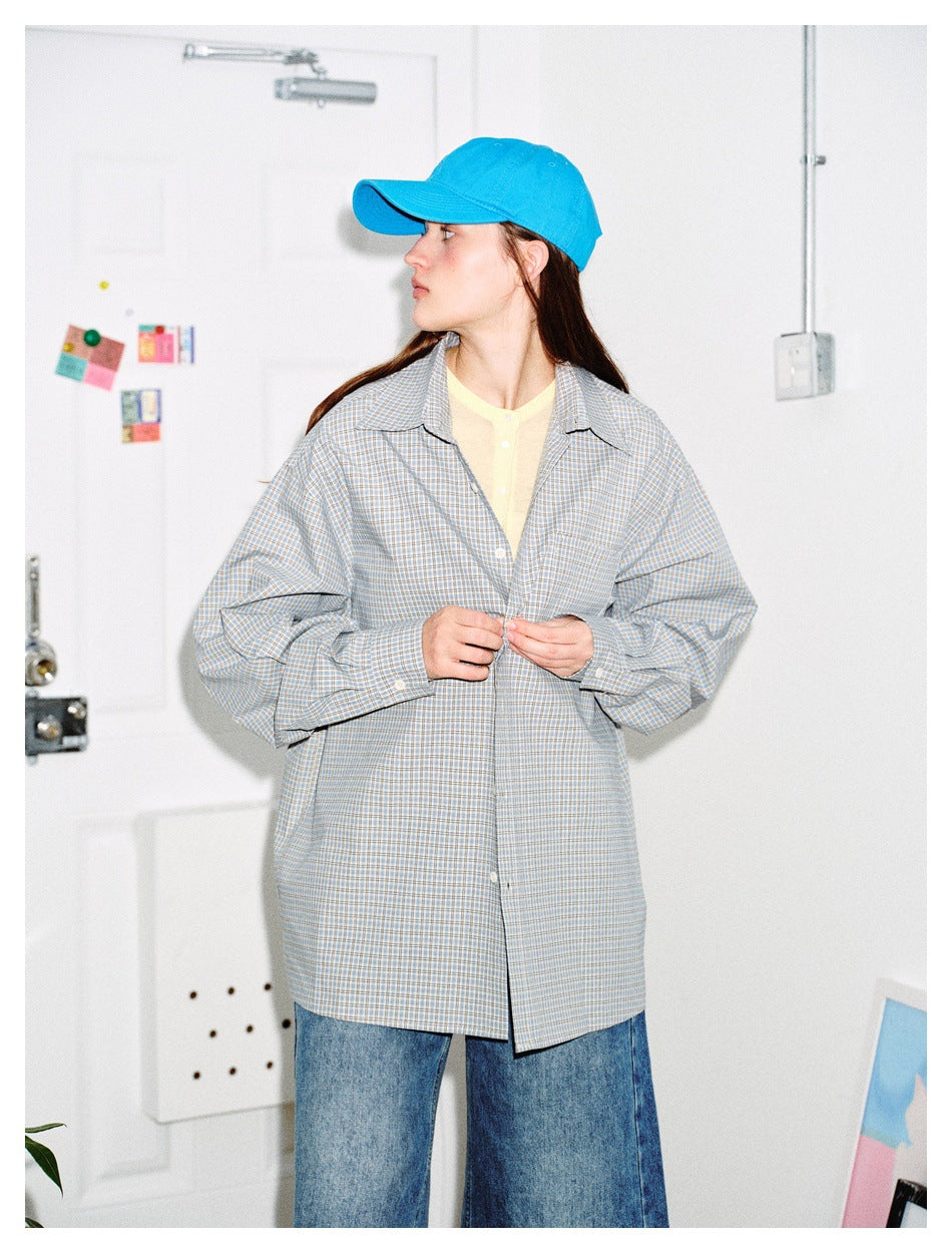 Model wearing a long, oversized gray-blue plaid button-up shirt with jeans and a bright blue cap.