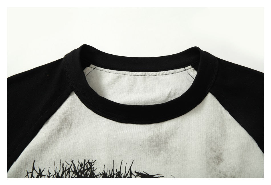 Close-up of the black ribbed crew neck and raglan seams on an off-white T-shirt with black sleeves.