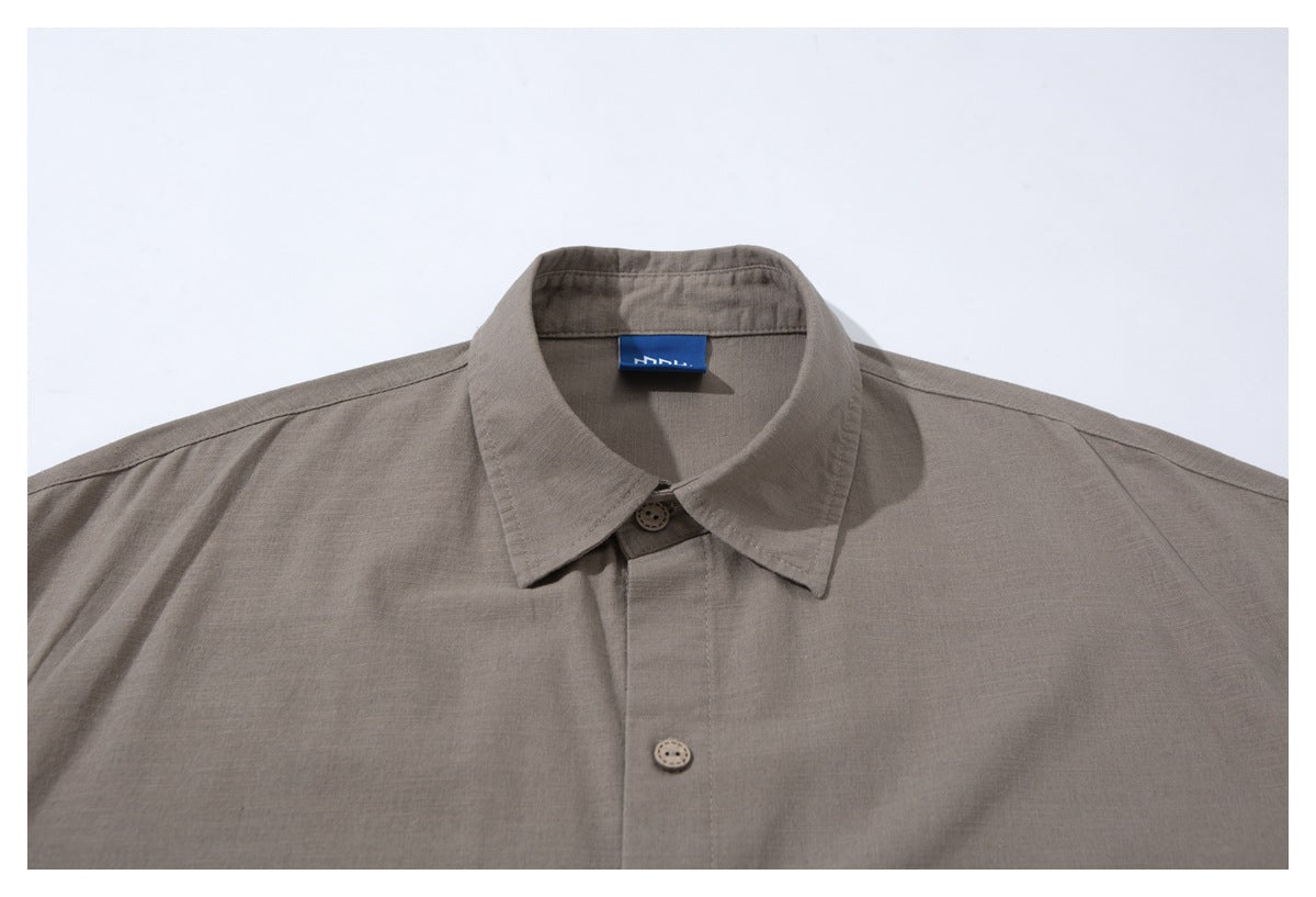 Close-up of a taupe button-up shirt showing its pointed collar, front buttons, and blue neck label.