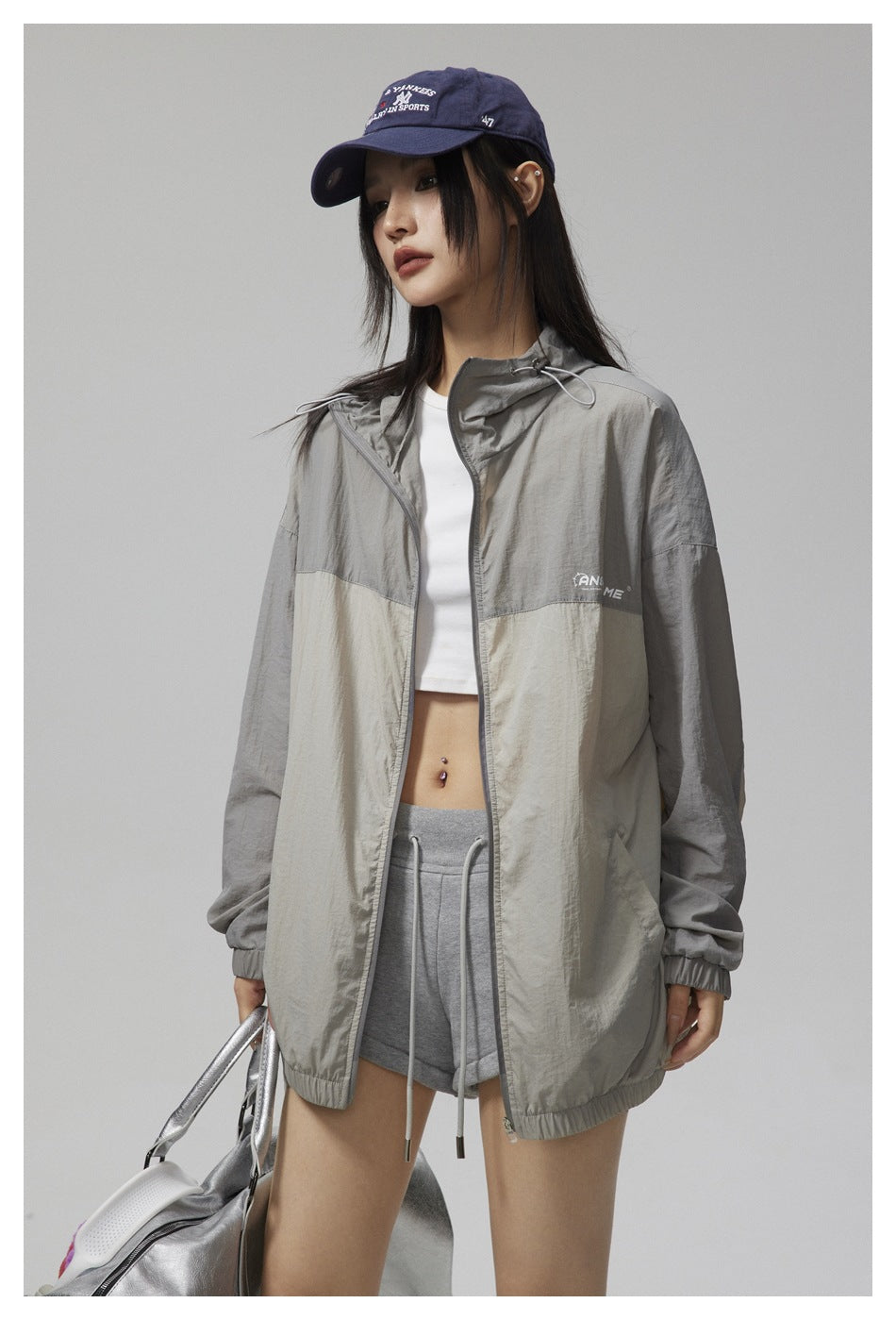 Closer view of a model wearing an open gray and cream color-block hooded jacket.