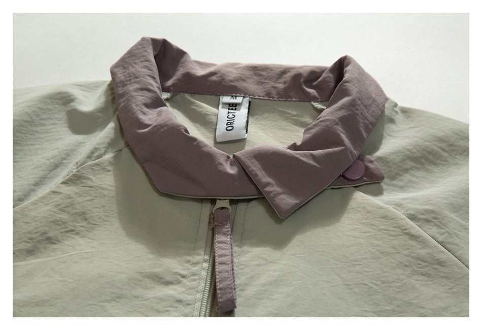 Close-up of a pale sage jacket with a wide dusty mauve collar, matching button and front zipper.