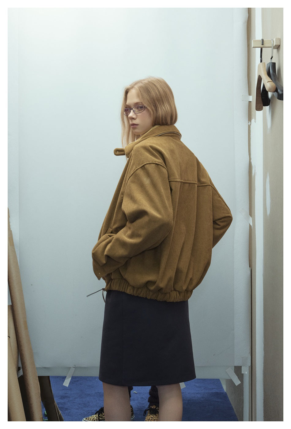 Model in a brown ribbed jacket, shown from the back with a dark skirt.