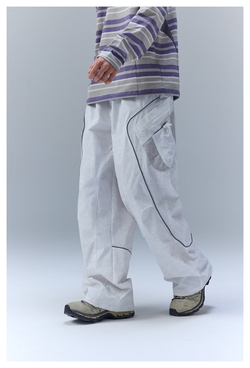 Side view of a model wearing light gray cargo pants with dark curved piping and a utility pocket.