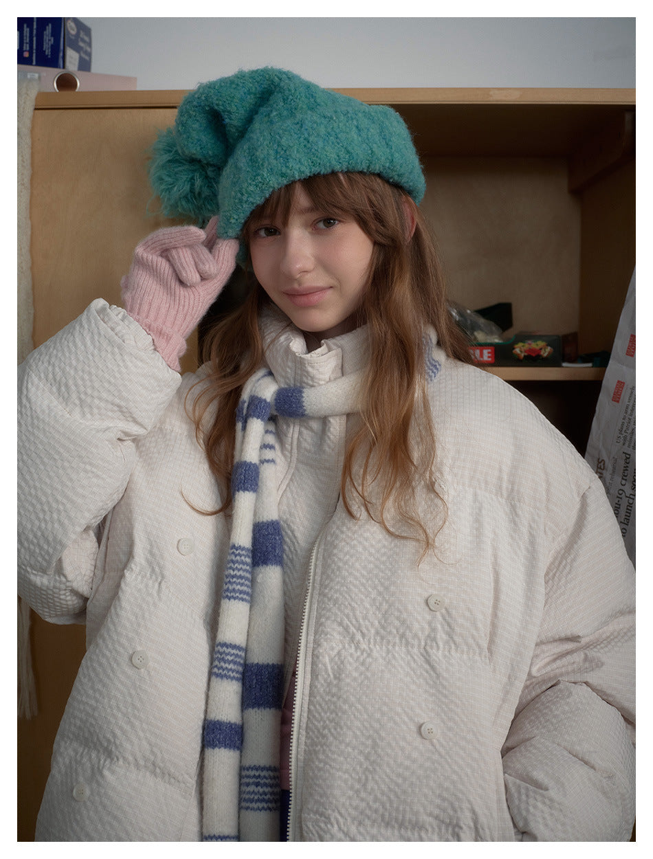Close view of a white quilted jacket with buttons, worn with a teal hat and blue-and-white scarf.