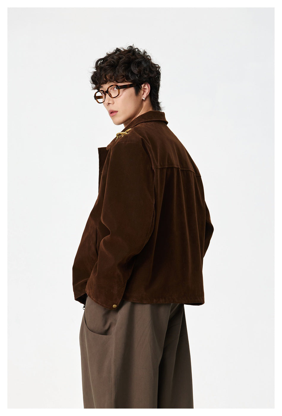 Model turned to show the back and side of a dark brown jacket with gold shoulder hardware.