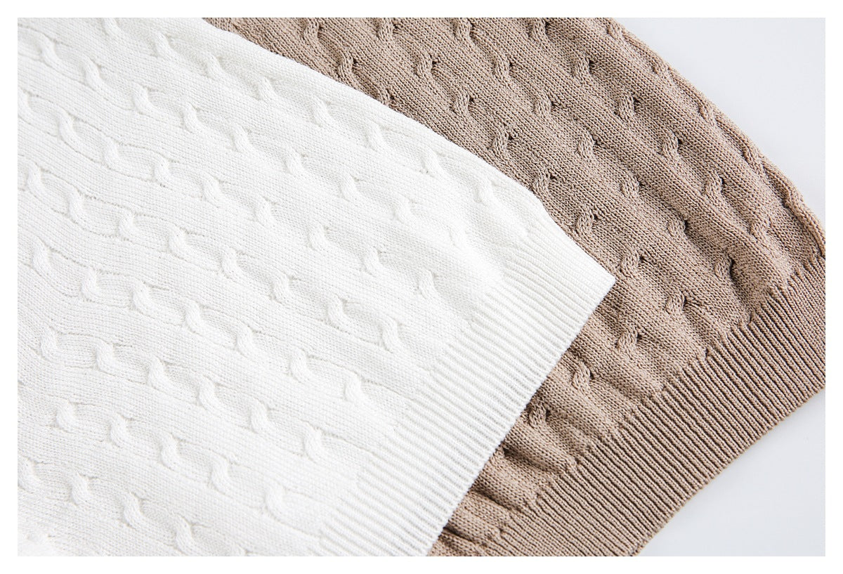 Close-up of ivory and taupe knit fabric with a raised repeating stitch pattern and ribbed edging.