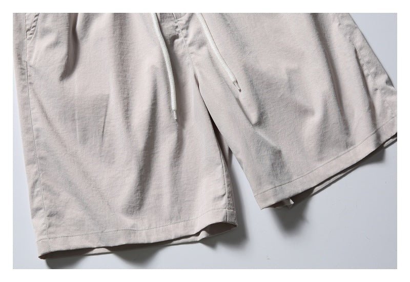 Close-up of the light beige shorts' straight legs, stitched hems, and hanging white drawcords.