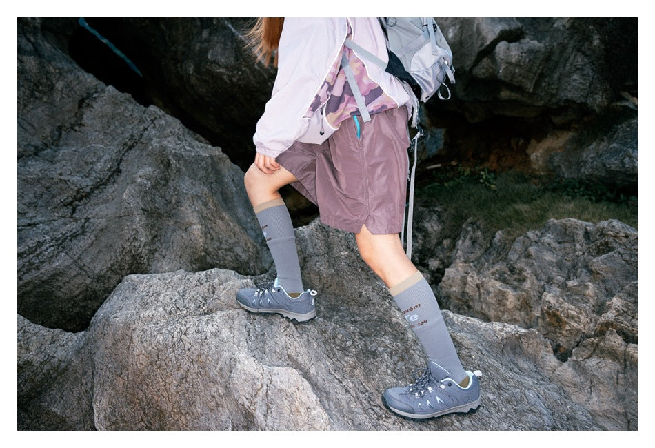 Rear-side view of mauve hiking shorts worn with a pale jacket as the hiker steps across rocks.